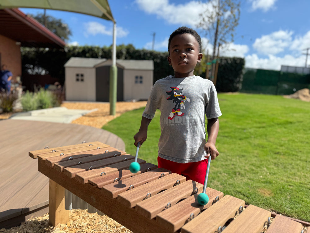 Child playing a wooden outdoor xylophone in a park setting
