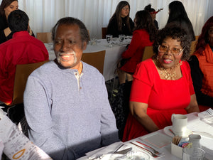 Elderly Afro American couple sitting down at a dining table.