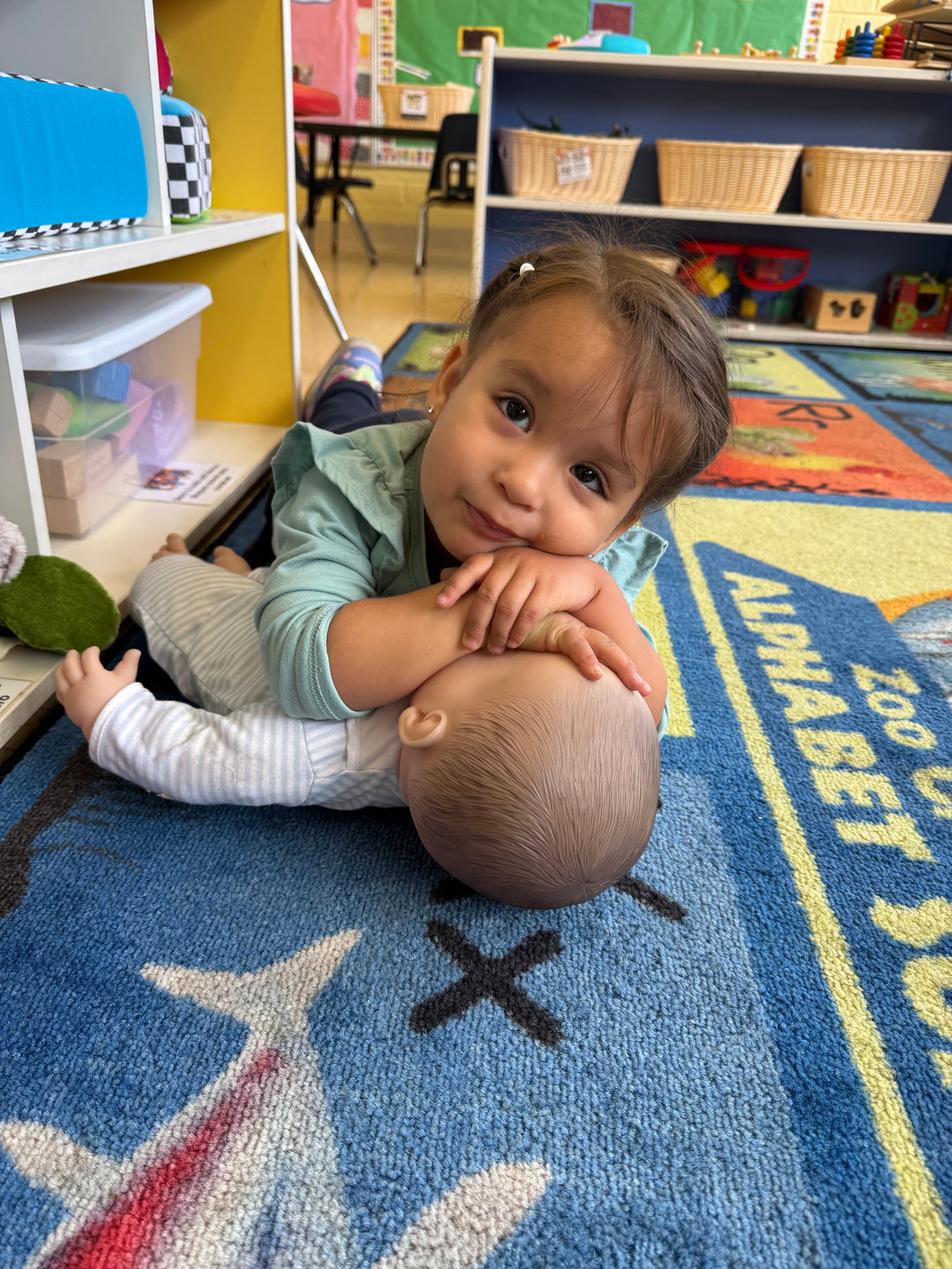 Child playing with a doll on a colorful classroom floor